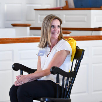 A woman smiles over her shoulder as she sits in a chair that represents the prize she has won for her work in the math department