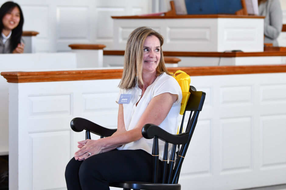 A woman smiles over her shoulder as she sits in a chair that represents the prize she has won for her work in the math department